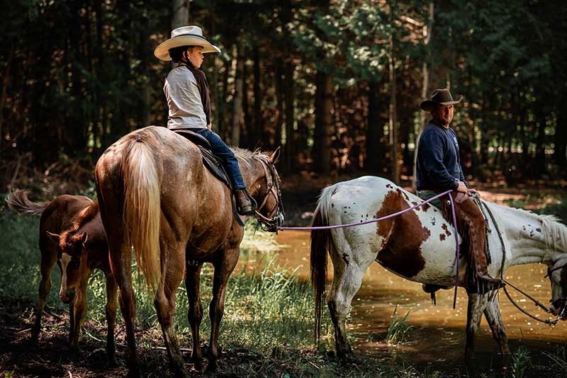 a trail hand on a horse holds a lead rope connected to a second horse with a young rider